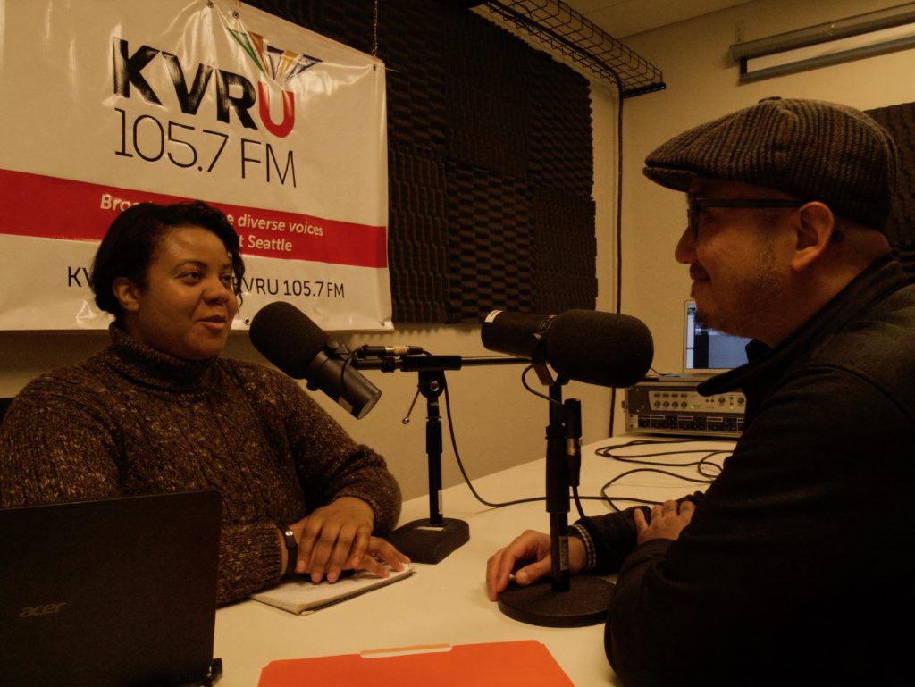 Photo of two people talking on microphone for the radio; photo from 2020 Arts & Culture Merit Award winner KVRU 105.7 FM