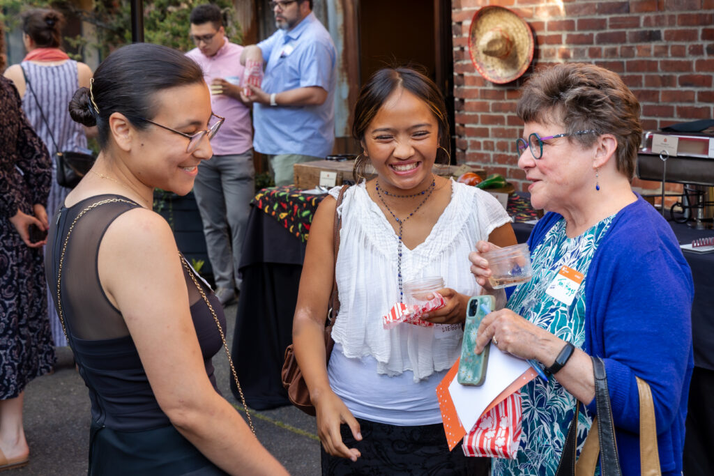 Three women standing outside having a joyful conversation. The woman in the middle is laughing.