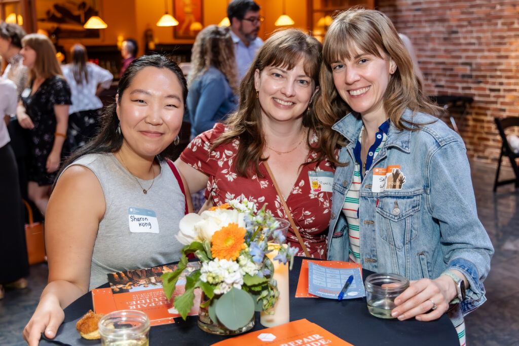 Three women standing around a table and smiling at the camera