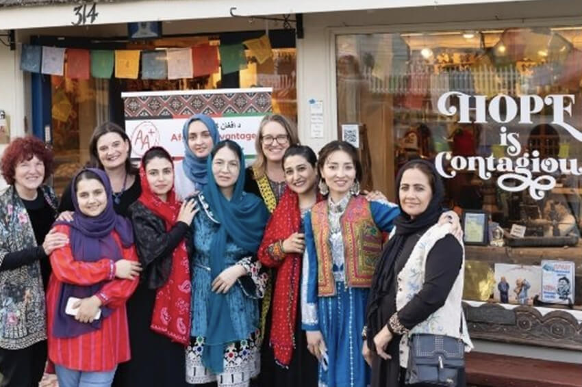 A group of women in colorful clothing standing in front of a store. The storefront window says "Hope is Contagious."